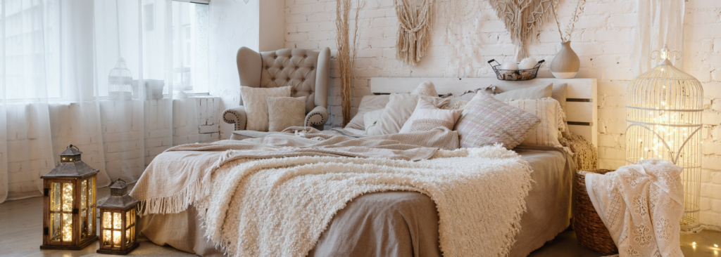 Seitenansicht eines Schlafzimmers mit Decken und Kissen auf Bett, Innendekor und Kissen auf einem Sessel in weißer Innendekoration im Boho Stil.